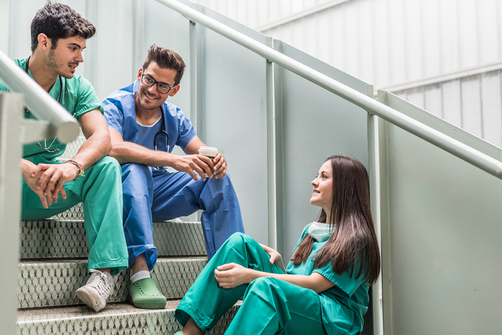 Junges medizinisches Personal sitzt auf Stiegen und redet.