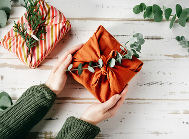 Furoshiki tissue wrapping of presents. Female hand holding a gift in eco friendly reusable fabric package. Small business, ethical shopping idea. Presents packed in plastic free. Zero waste lifestyle
