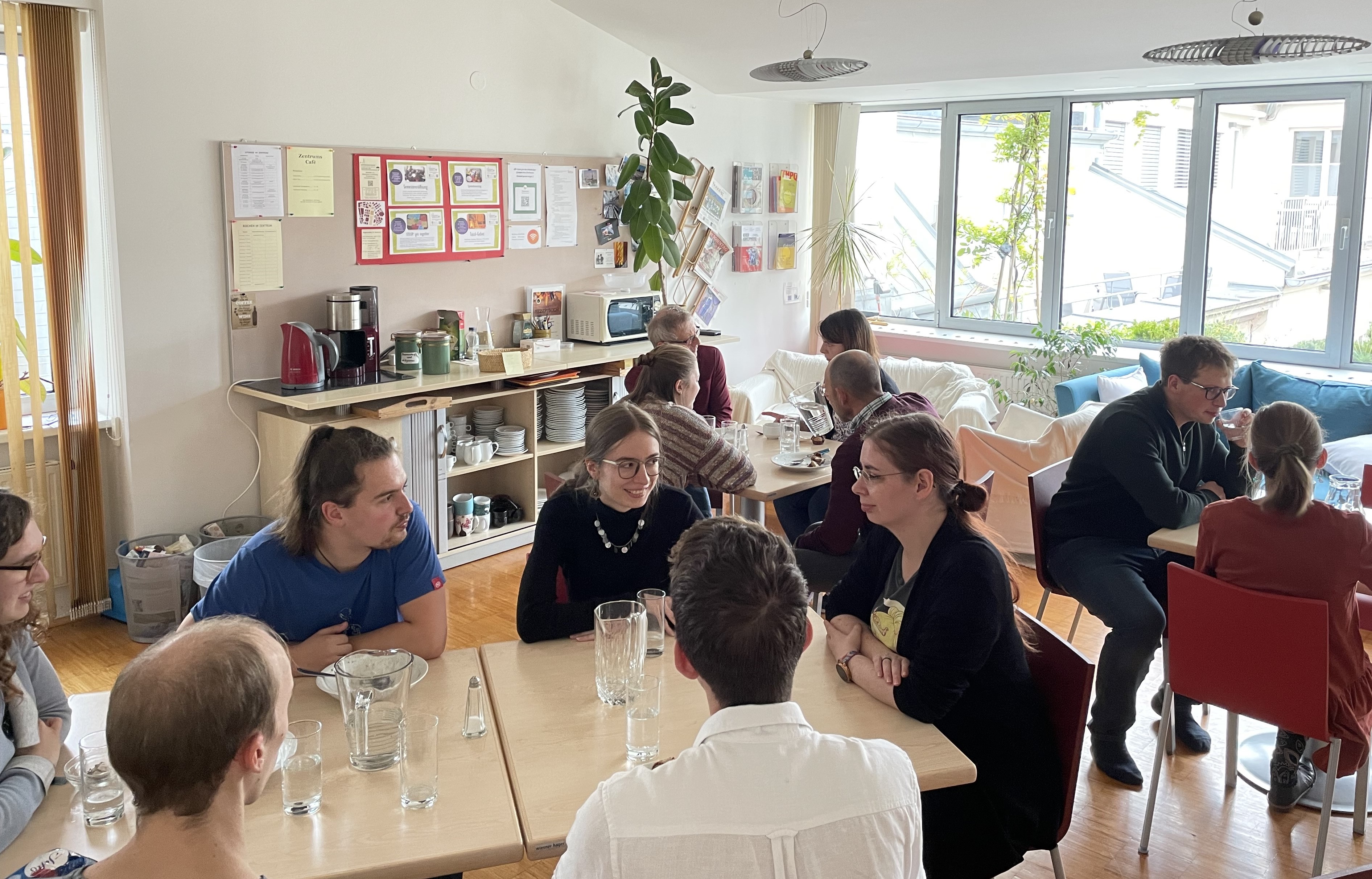 Im Zentrum sitzen mehrere Studierende um Tische und reden und essen gemeinsam zu Mittag.