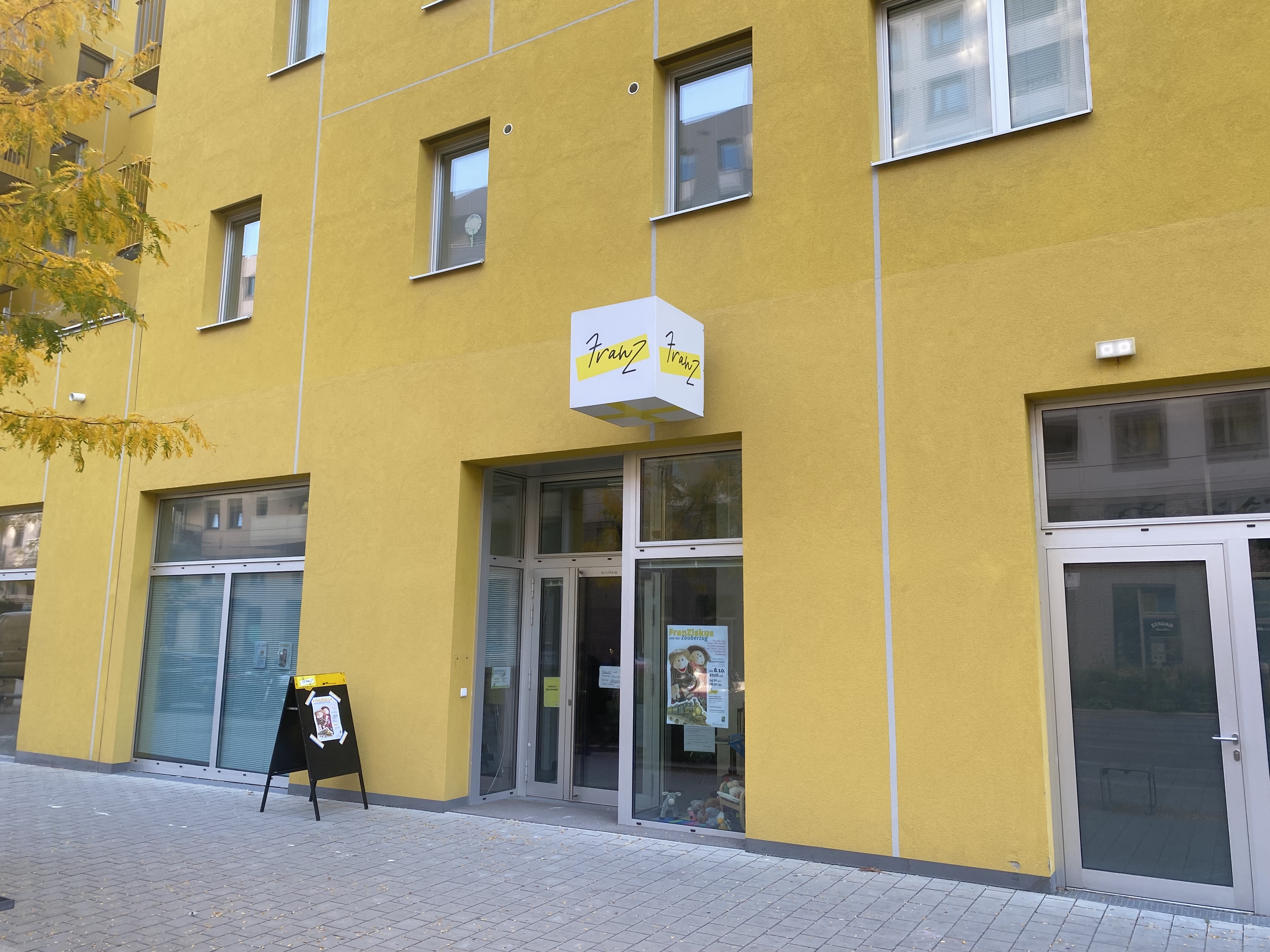Eingang von Franz: gelbe Hausfassade mit würfelförmigem Schild und gelb hinterlegtem Franz-Logo