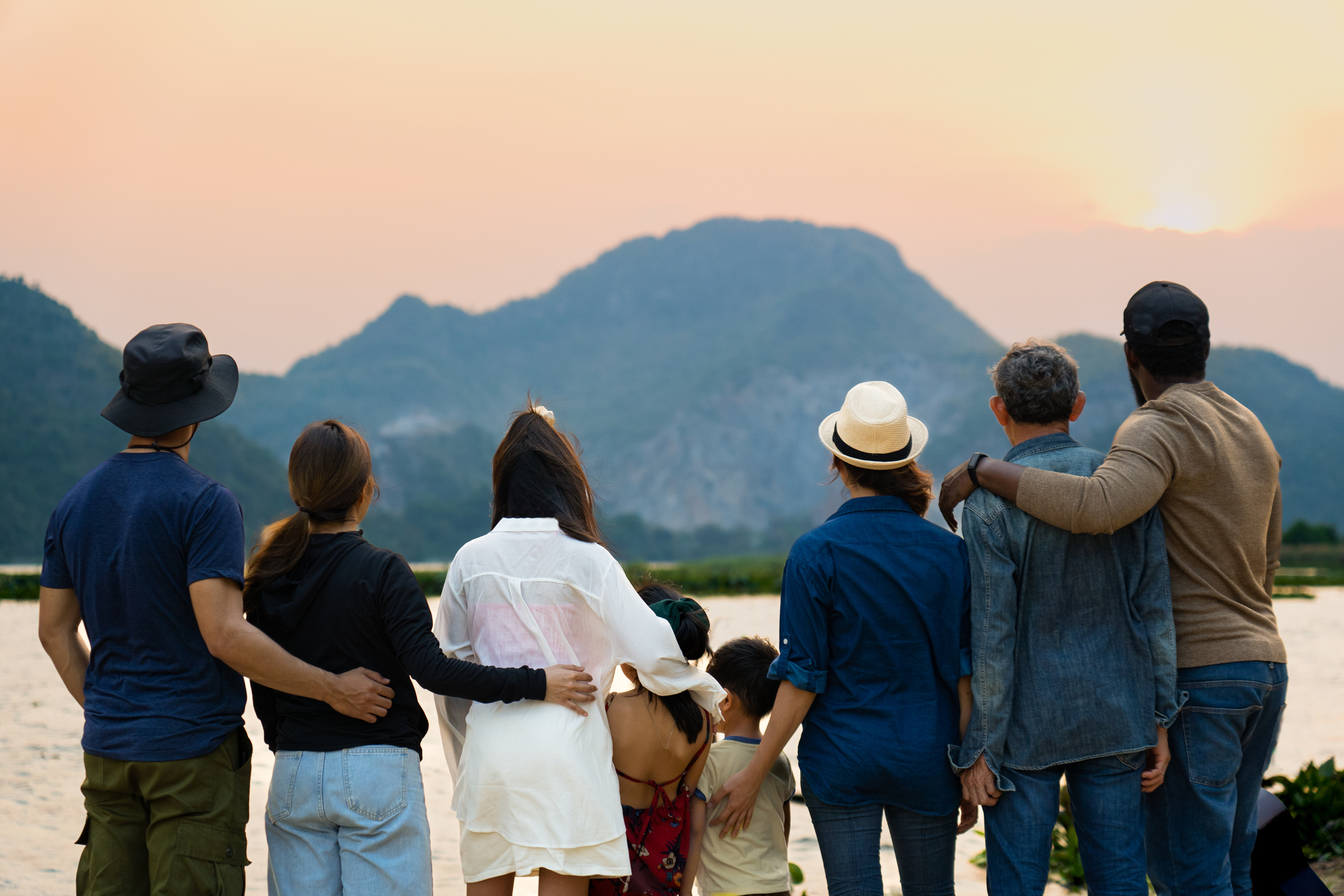 back view of happy family standing and looking at sunset behind the mountain and river beauty in nature at camping area, multi-generation travelers spend time together during weekend holiday vacation