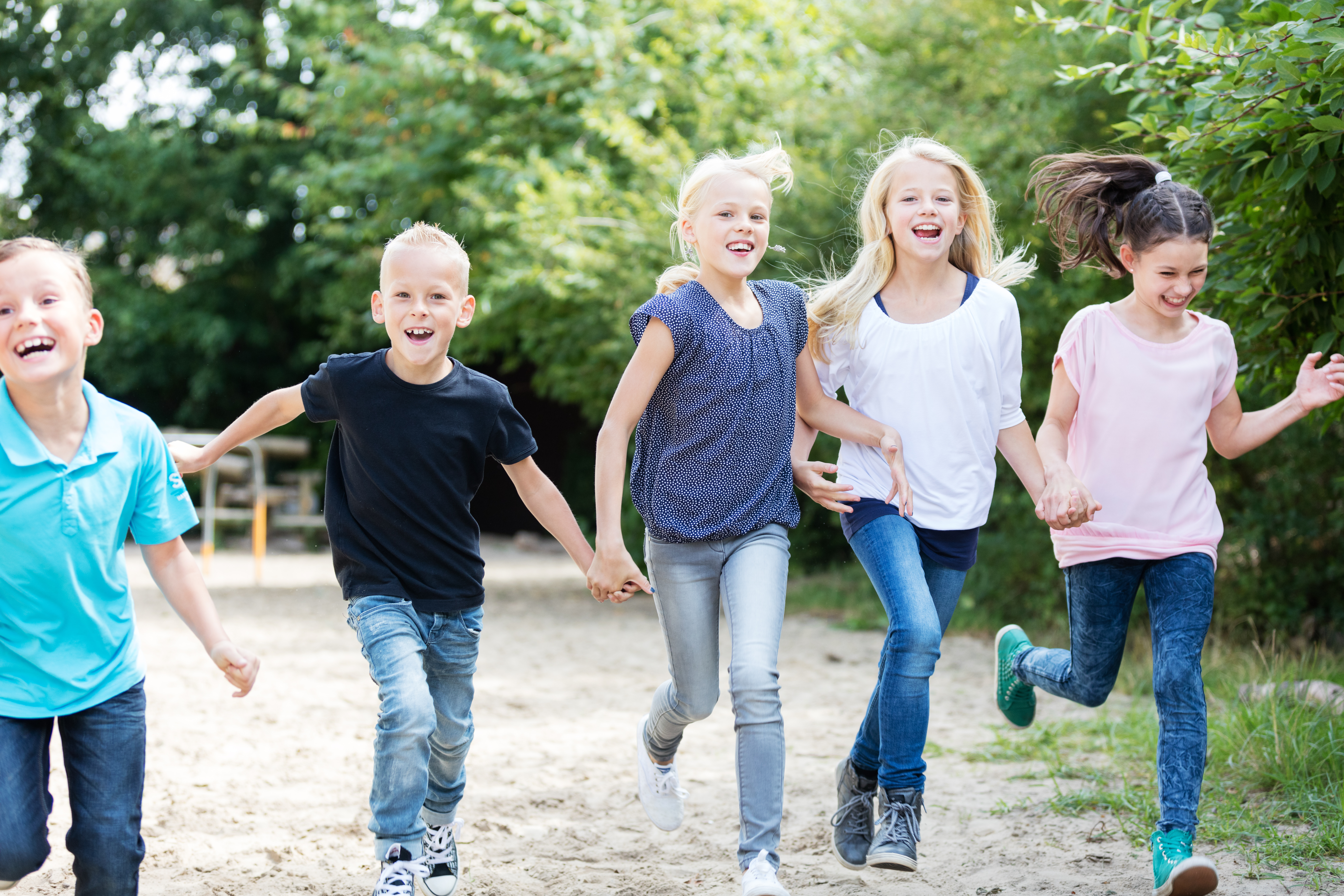 Mehrere lachende Kinder laufen gemeinsam auf einem Weg im Freien