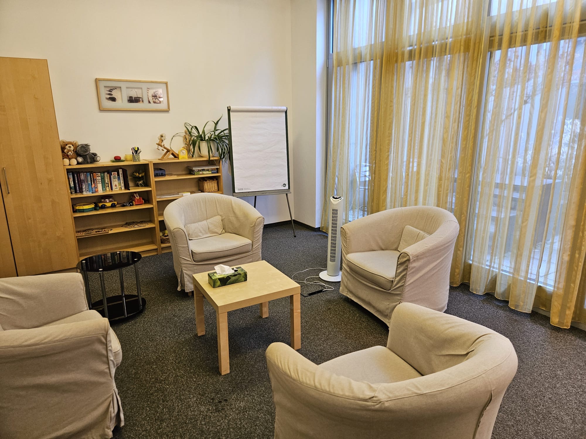 Heller Raum mit drei Sesseln, Holztisch und Flipchart