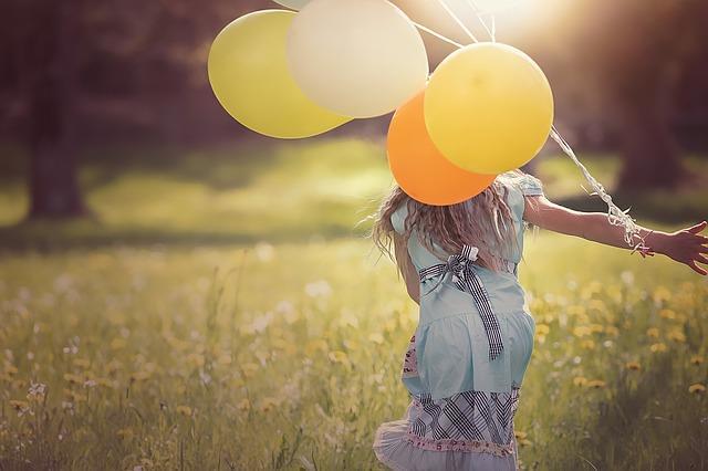 Mädchen läuft mit Luftballons über eine Wiese.