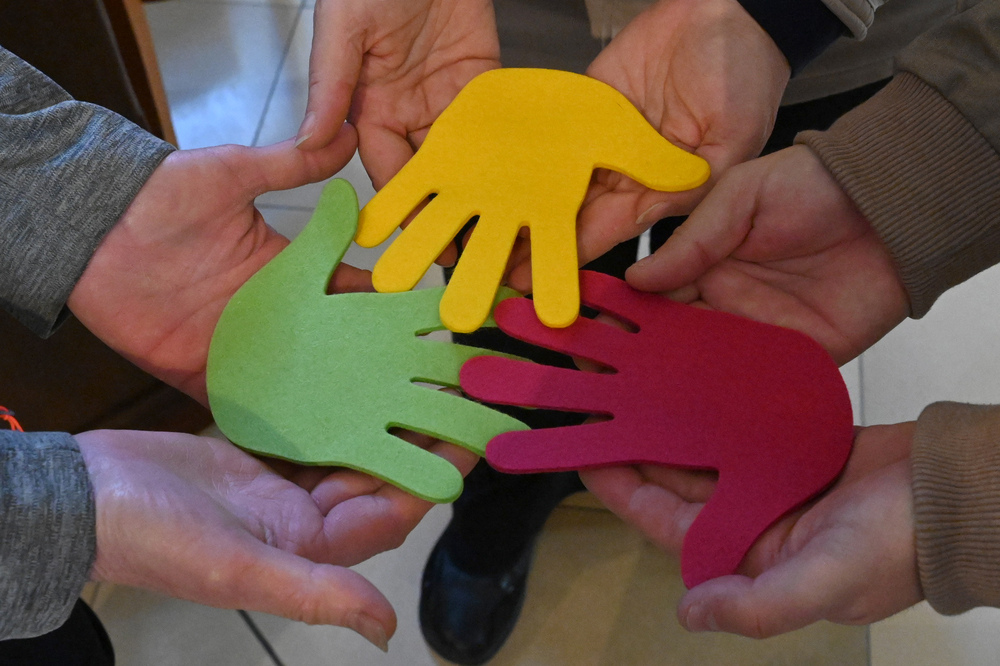 Menschen halten drei verschiedene bunte Hände als Symbol für Zusammenarbeit, Zusammenhalt und Gemeinschaft.