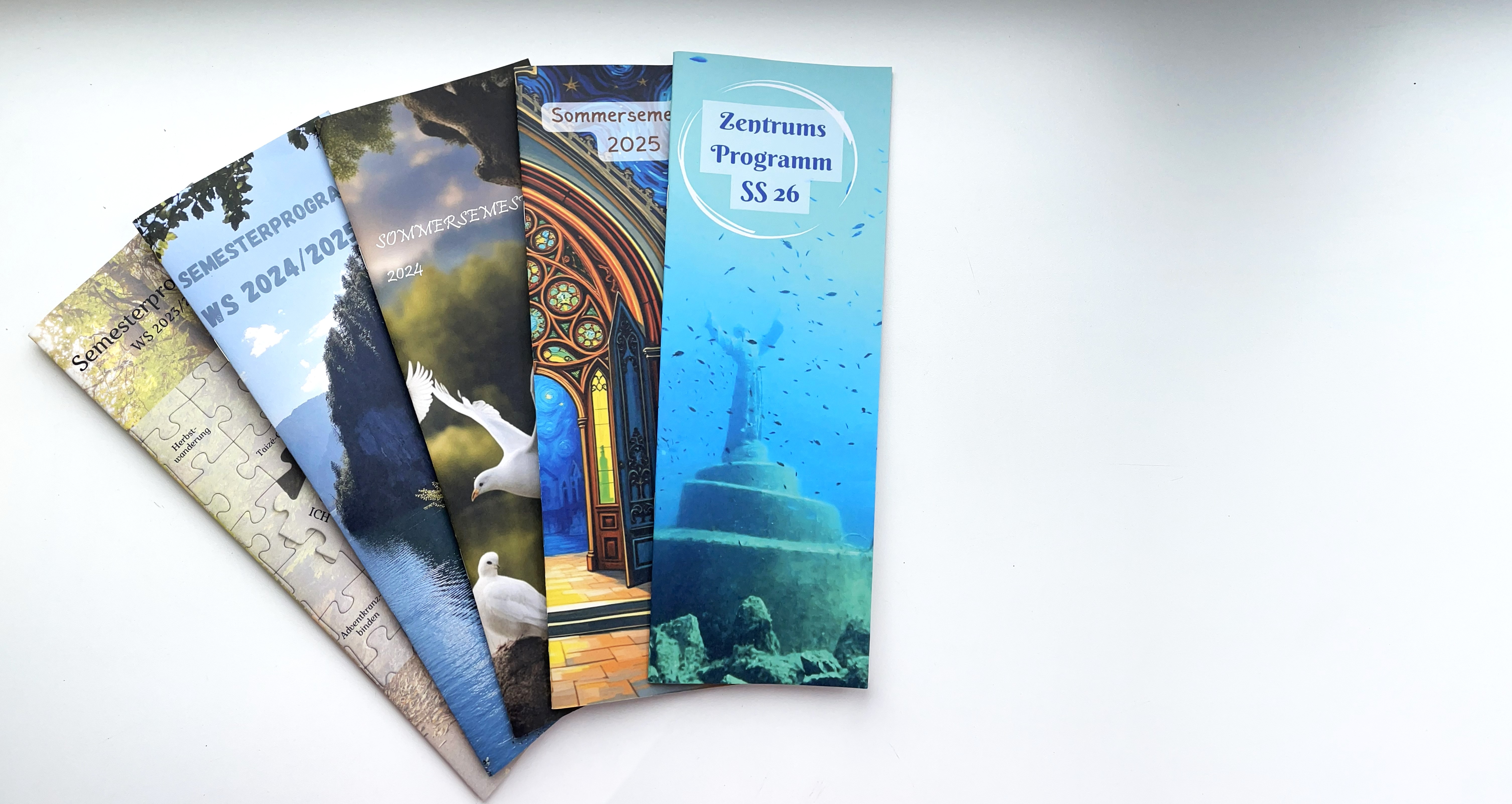 Auf dem Bild sind vor weißem Hintergrund fünf alte Semesterprogramme aus vergangenen Jahren vom Zentrum für Theologiestudierende abgebildet.
