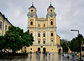 Mondsee, Austria - 05.08.2016: Basilica St. Michael, a yellow and white church building, a clock is installed on the towers, the square is covered with white and black tiles, trees grow nearby.