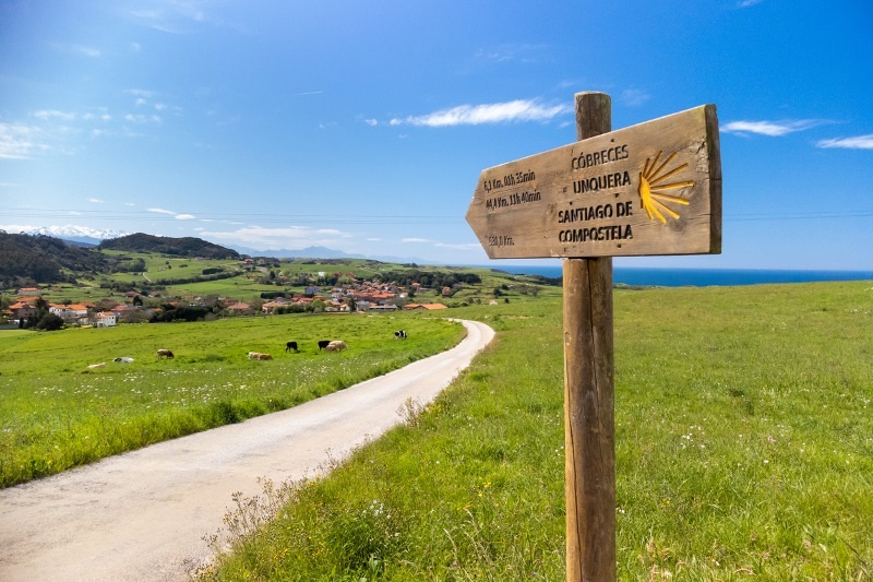 Wooden milestone indicating kilometers to Unquera and Cobreces during the route of the Camino de Santiago.