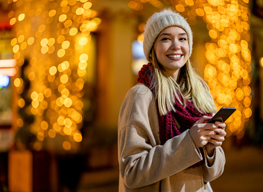 Portrait of beautiful young woman using her mobile phone in the street with christmas decoration on background
