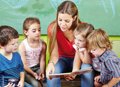 Erzieher und viele Kinder in einer Gruppe lesen ein Buch im Kindergarten