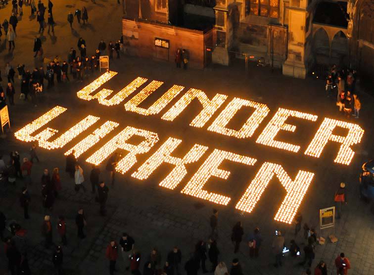 Schriftzug aus Kerzenlichtern: 'Wunder wirken'; Caritas-Aktion