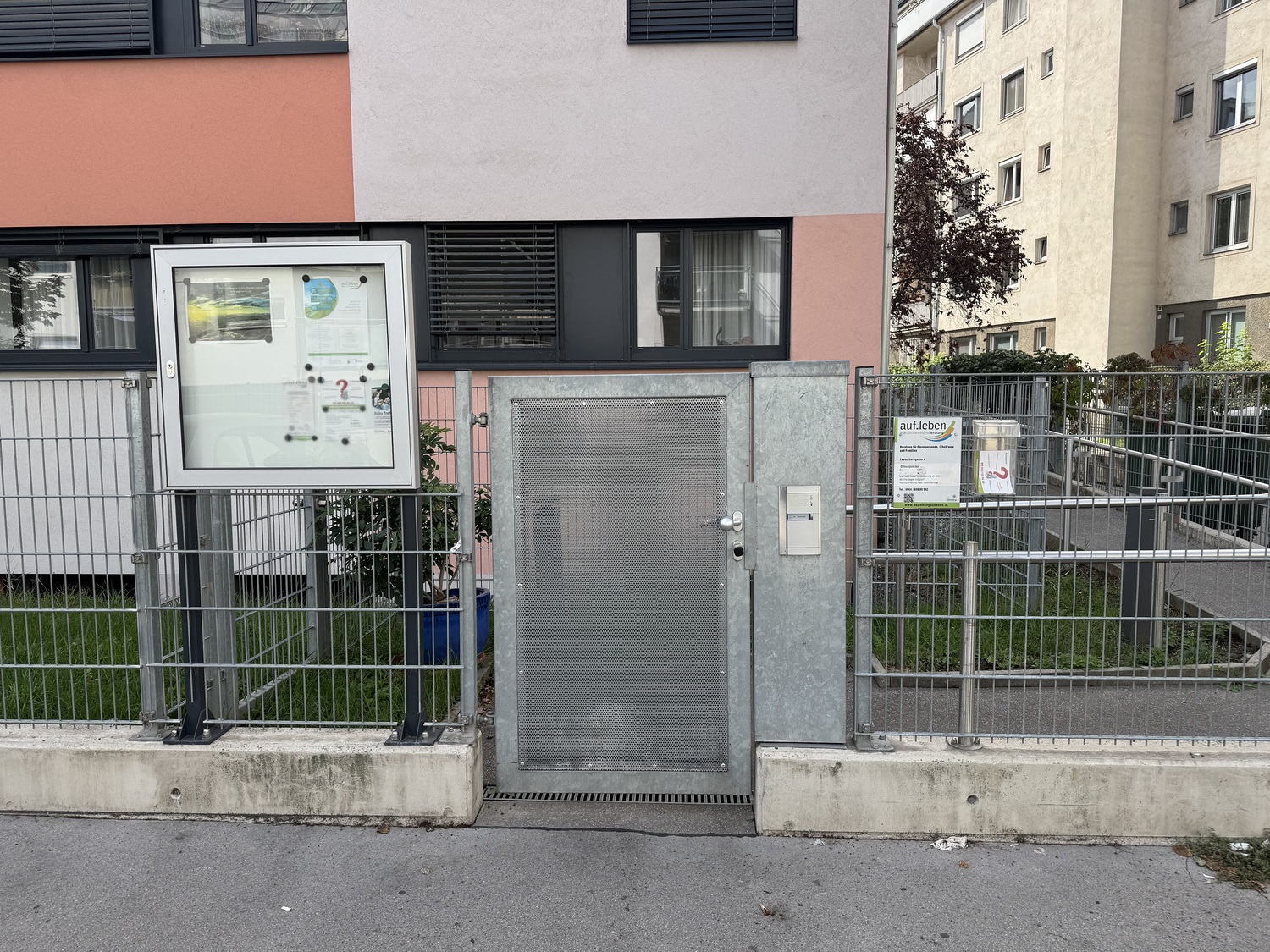 Eingang zur Beratungsstelle: ein verzinktes Metalltor mit Gegensprechanlage, links ein Schaukasten, rechts ein Schild mit der Aufschrift „auf.leben“, davor der Gehsteig.