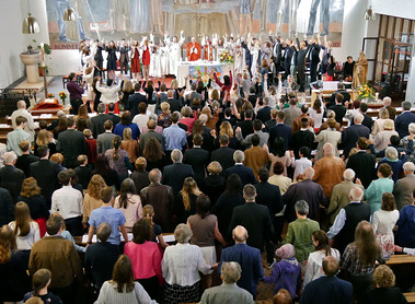 Zum gesungenen Vater Unser stehen die Firmlinge und FirmbegleiterInnen um den Altar und die Leute in den Reihen reichen sich Hände.
