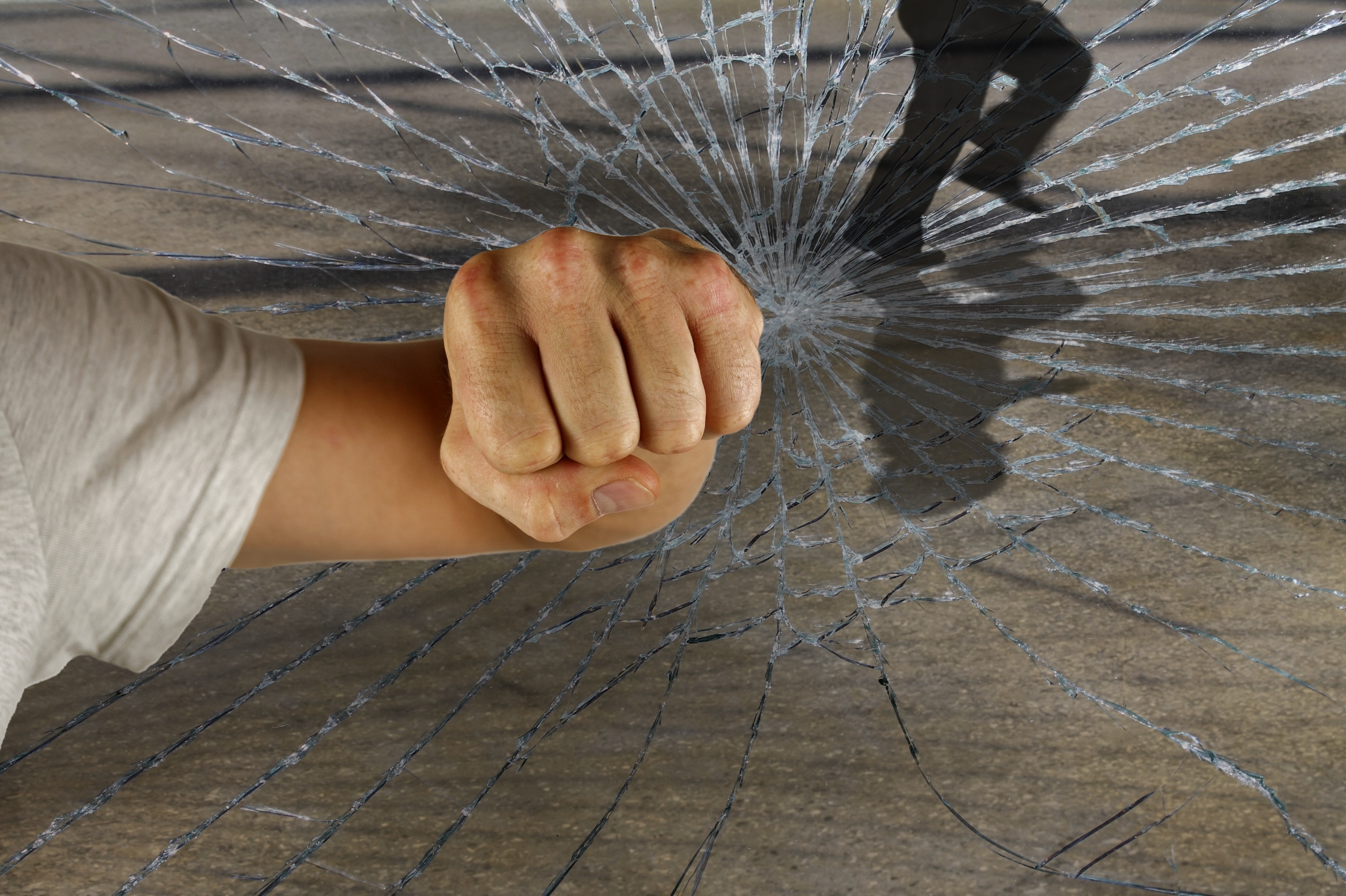 Eine geballte Faust durchschlägt eine Glasscheibe, die in viele Risse zerspringt