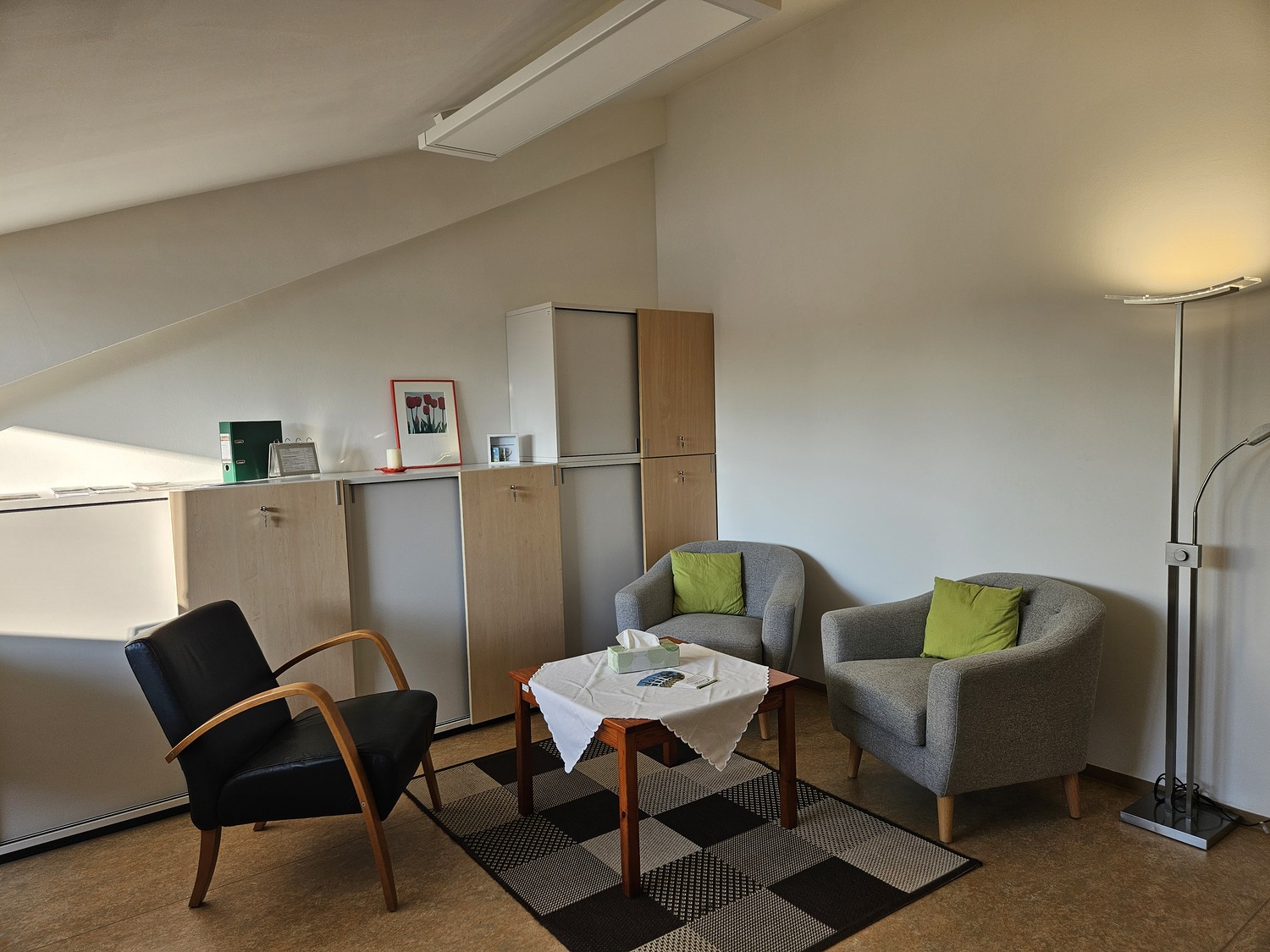 Heller Dachraum mit drei Sesseln, Holztisch und Schränken