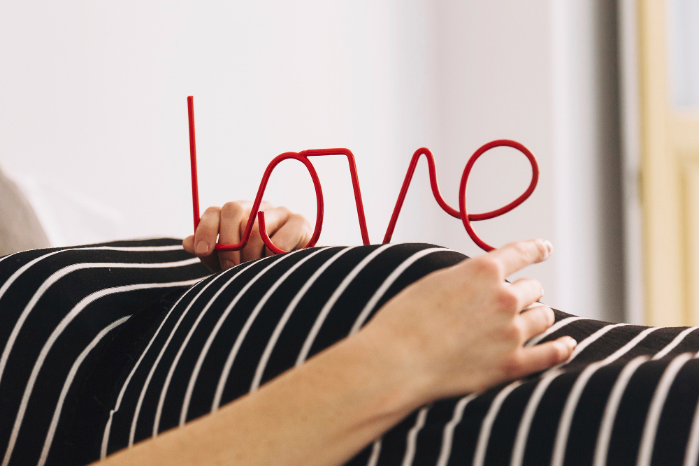 Schwangere Frau hält auf dem Bauch die Buchstaben für LOVE in der Hand