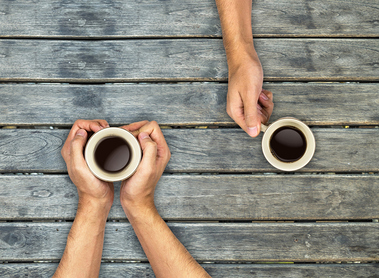 Coffee mugs hands holding on wood table, top view angle