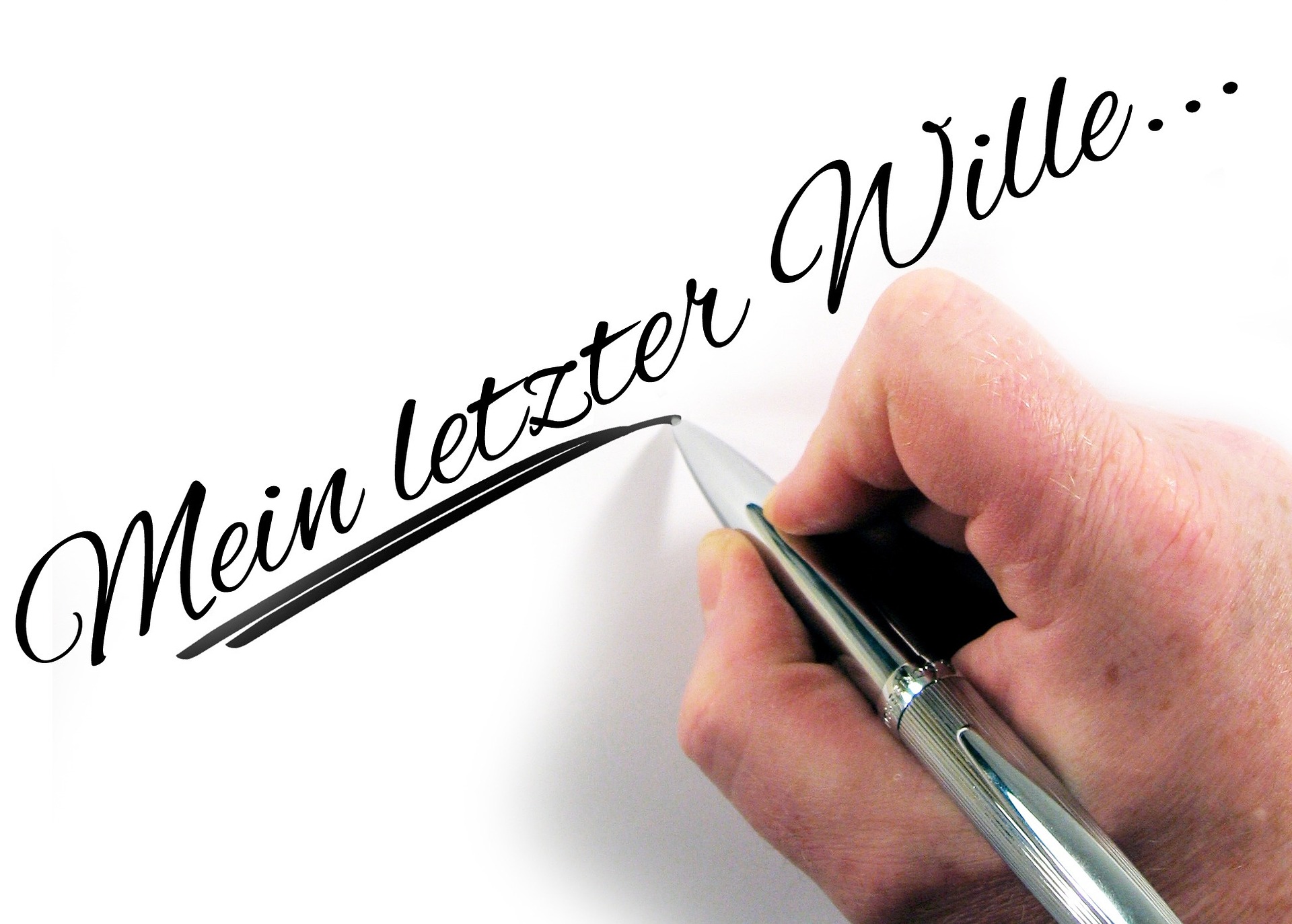 Eine Hand schreibt mit einem Stift die Worte 'Mein letzter Wille' auf weisses Papier