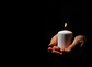 Woman holds candle on black background, space for text