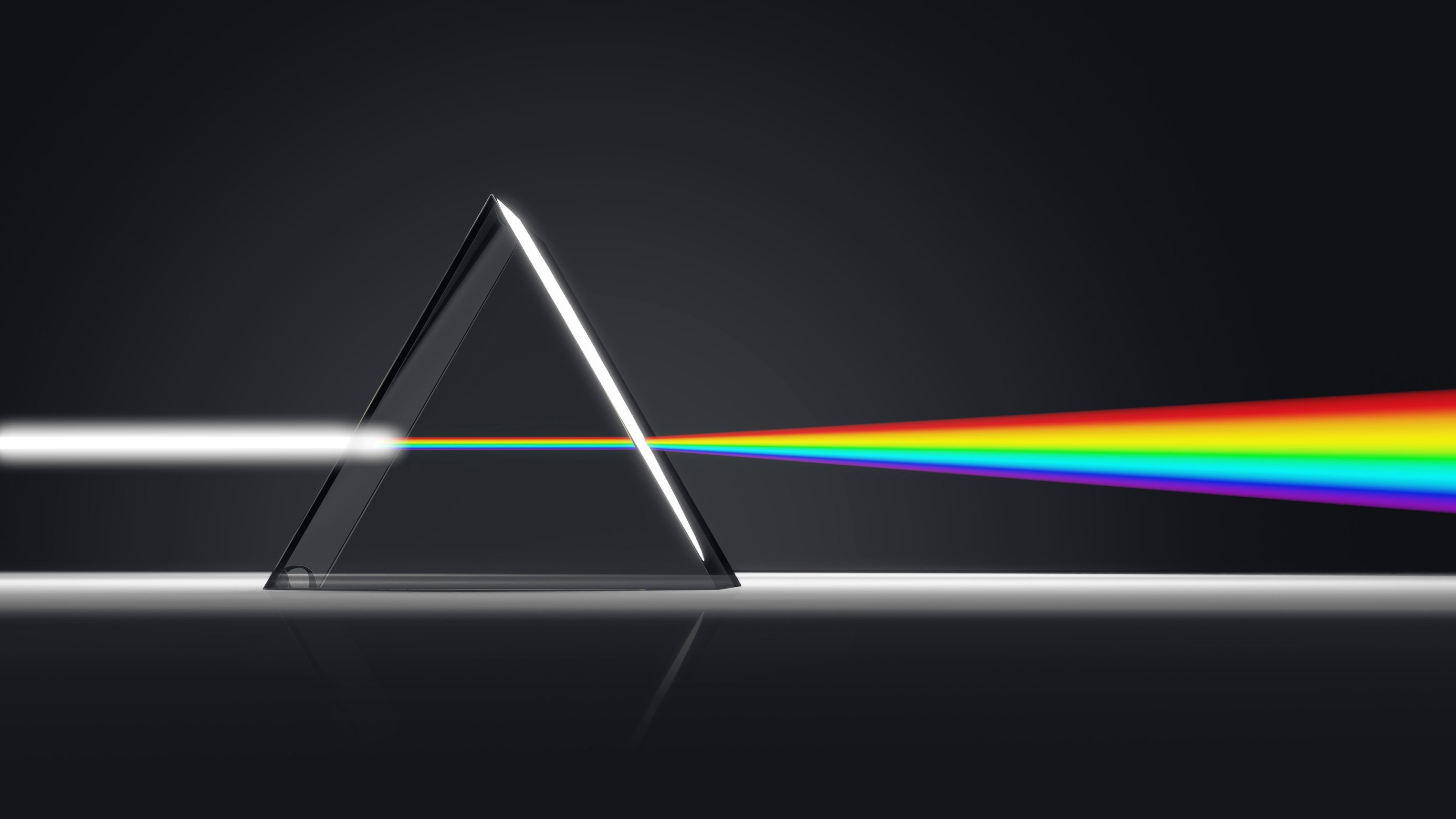Ein weißer Lichtstrahl trifft auf ein Prisma und fächert sich in Regenbogenfarben auf