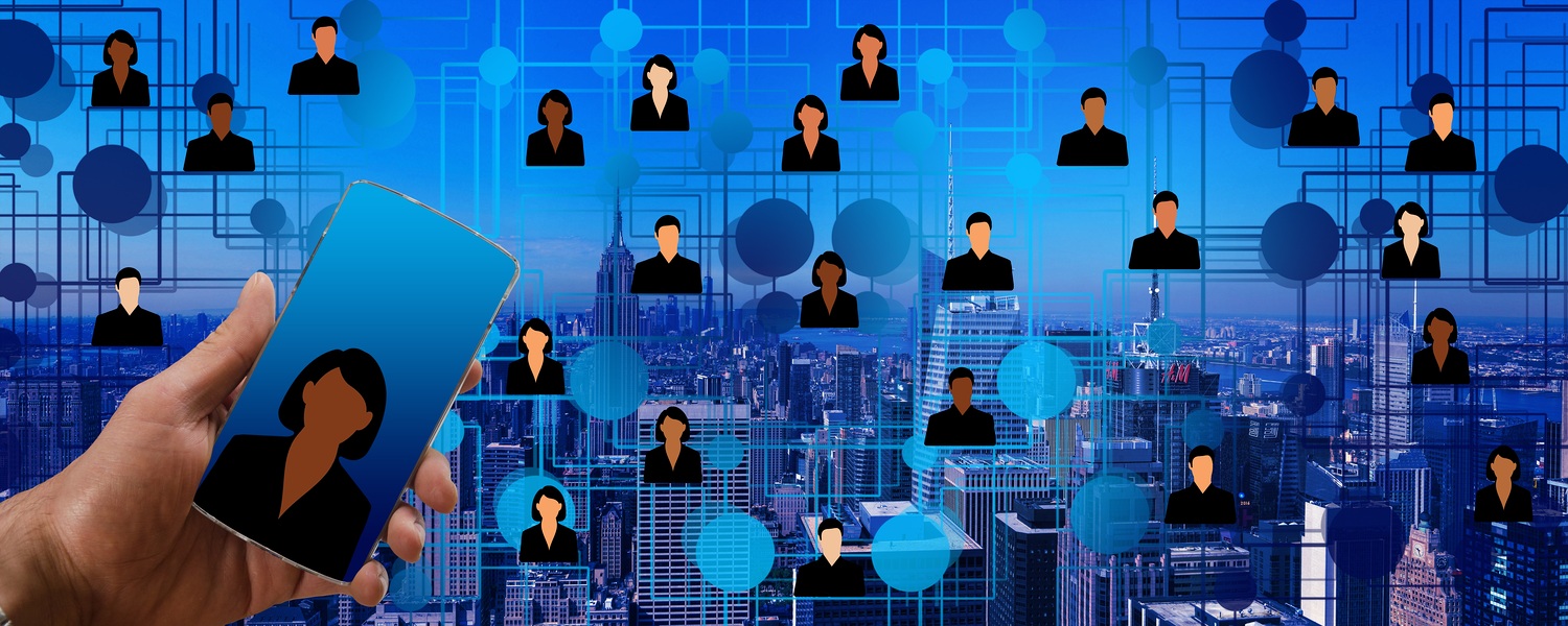 Eine Hand hält ein Smartphone vor einer Skyline, darüber schweben vernetzte Personensymbole als Sinnbild für digitale Chatberatung