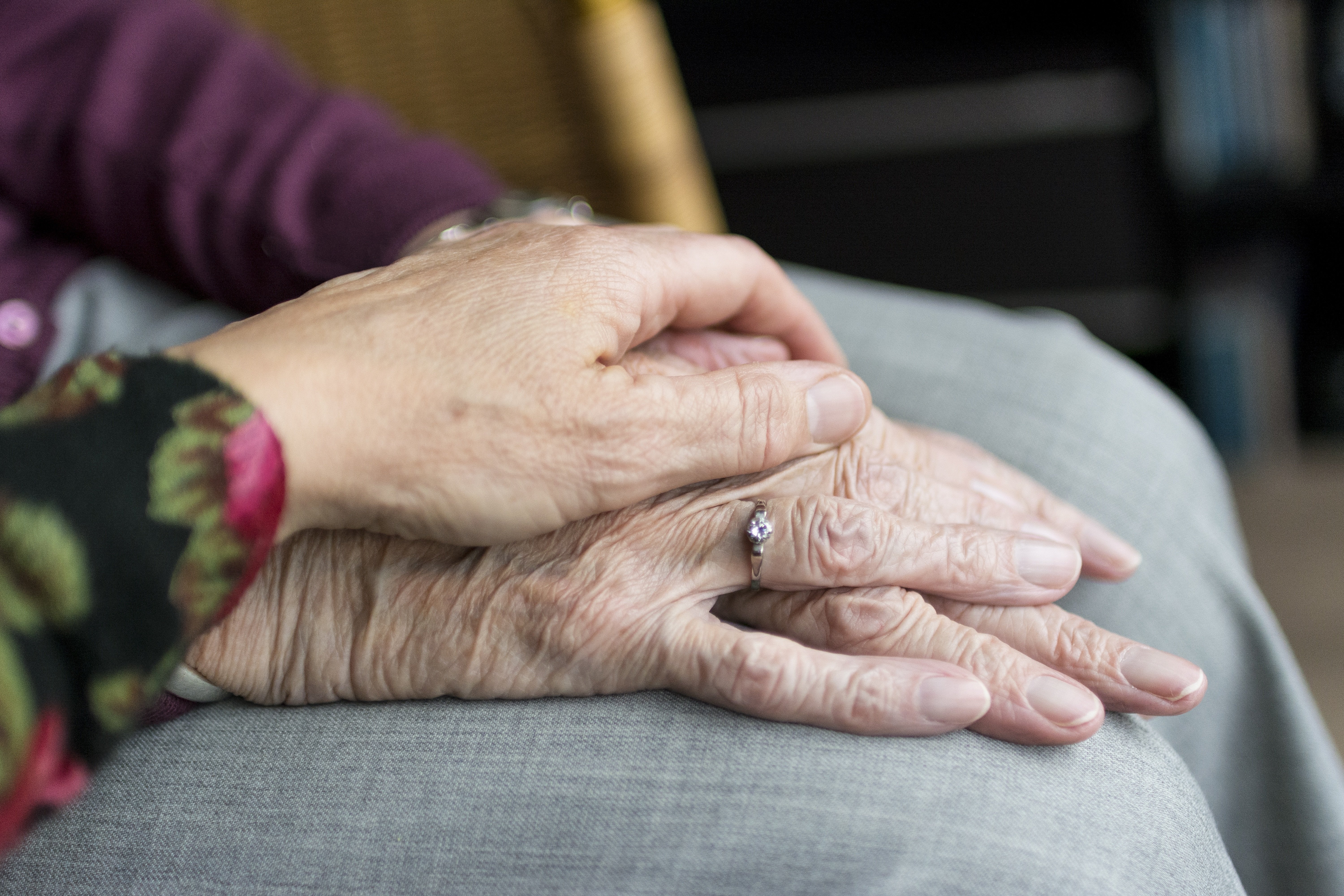 Eine Hand liegt tröstend auf den gefalteten Händen einer sehr alten Person