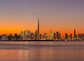 Panorama of Dubai Business Bay skyline at night after sunset with colorful illuminated buildings and calm Dubai Creek water.
