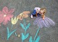 Little preschool girl painting with colorful chalks flowers on ground on backyard. Positive happy toddler child drawing and creating pictures on asphalt. Creative outdoors children activity in summer