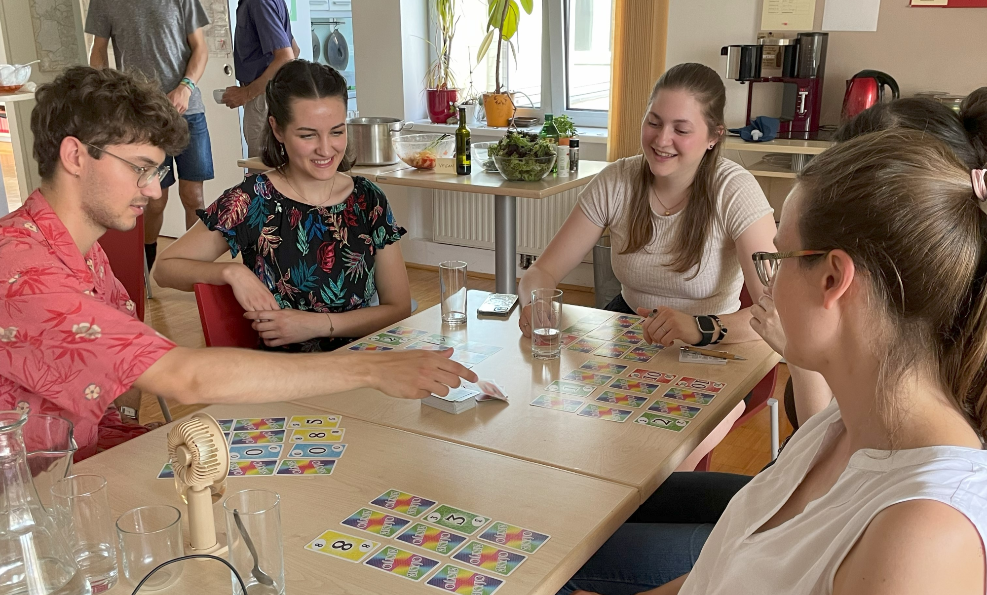 Auf dem Bild sieht man eine gruppe von jungen Menschen, die um einen Tisch sitzen und Skippo, ein Kartenspiel, spielen. 