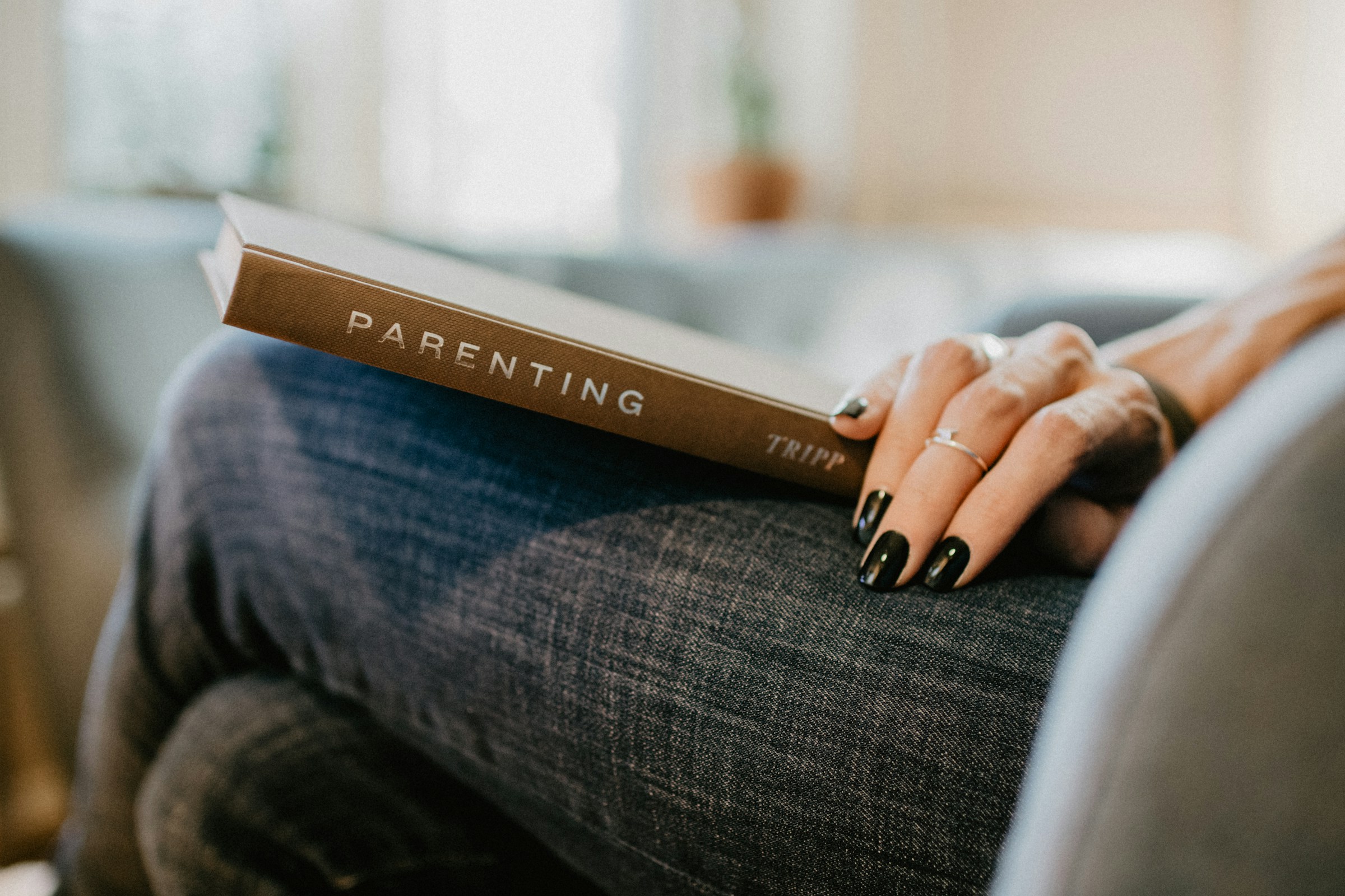 Eine Frau sitzt im Sessel und hält ein Buch mit dem Titel „Parenting“ auf dem Schoß