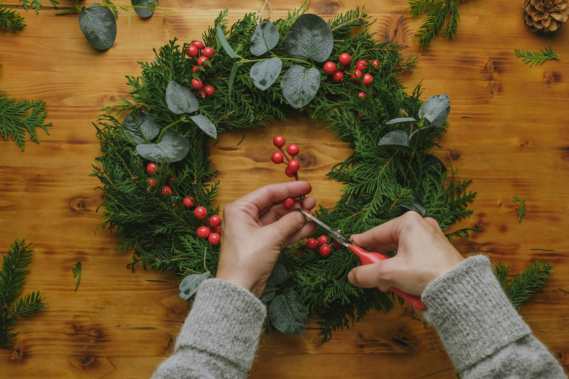 Hands making Christmas wreath with holly berries. DIY Christmas decoration.