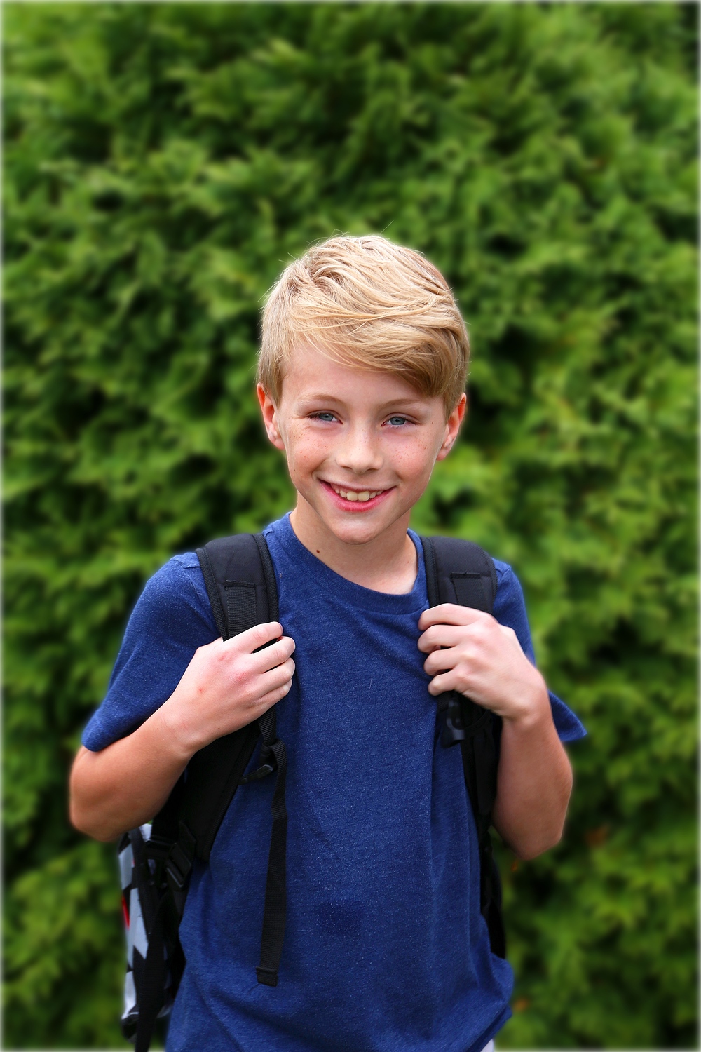A happy young boy child is smiling as he wears his backpack on his first day of school in 4th grade.